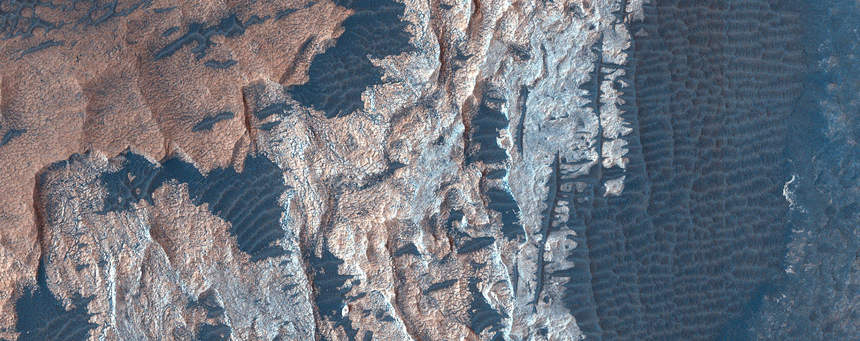 Mars from orbit. Pinkish rocky terrain with ripped textured grey sand filling in gaps.